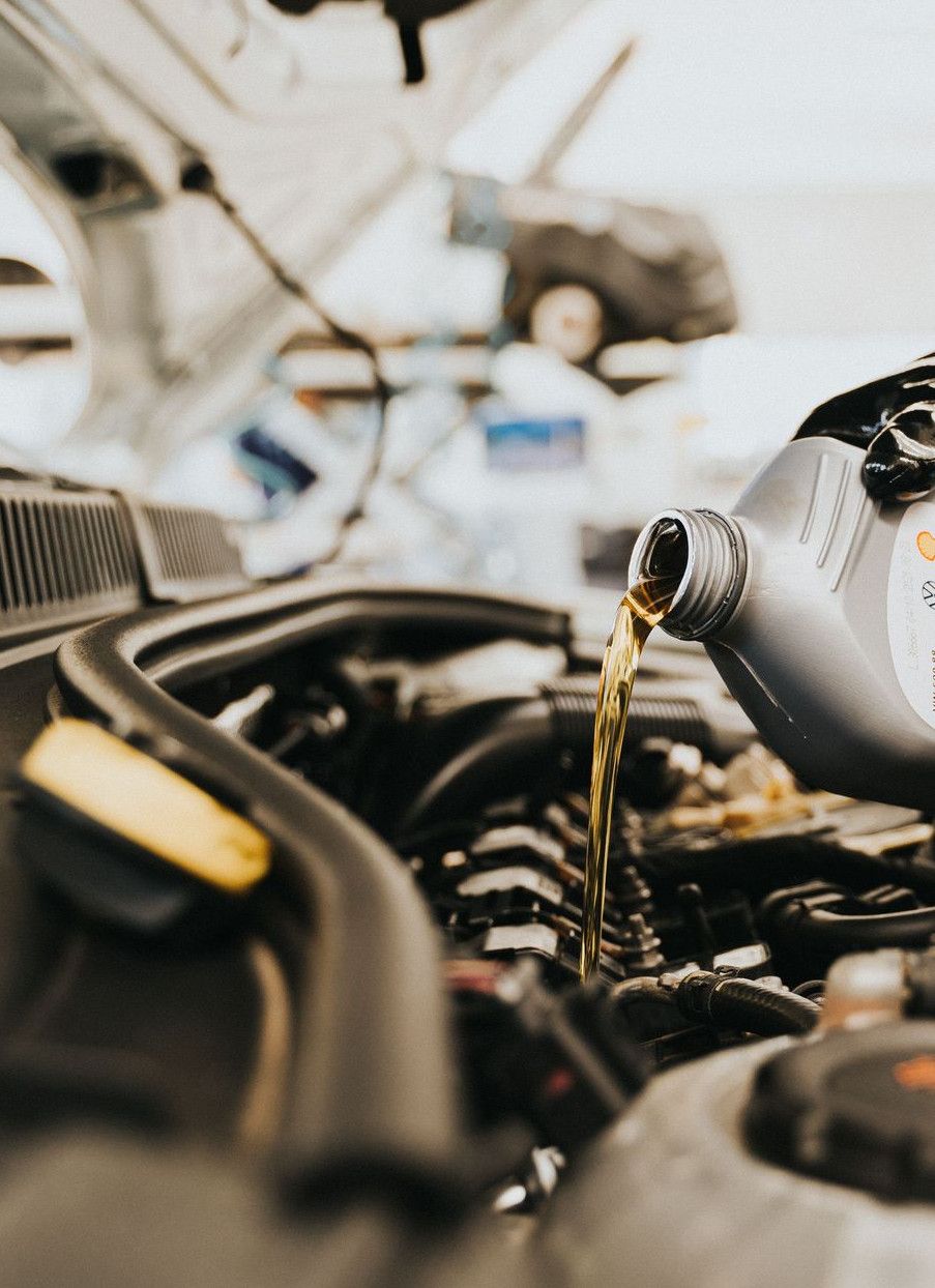 Close-up of a mechanic pouring engine oil into a car engine in an auto repair shop.