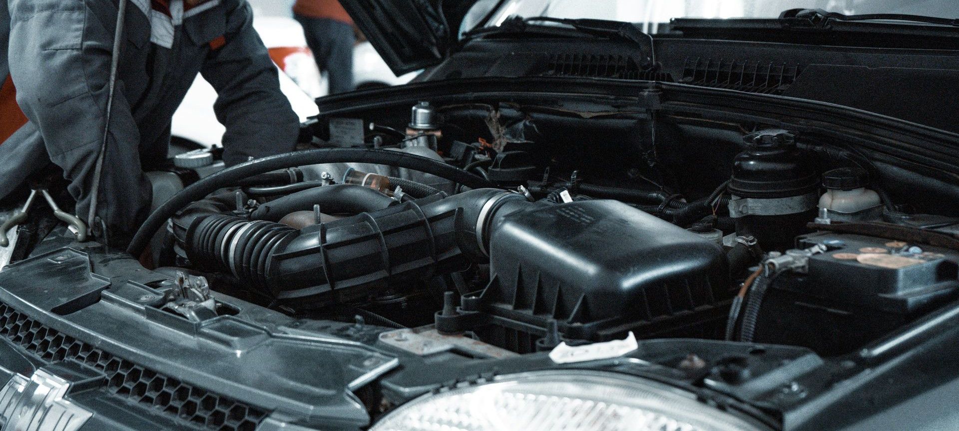 A mechanic in a grey uniform inspecting the engine of a car